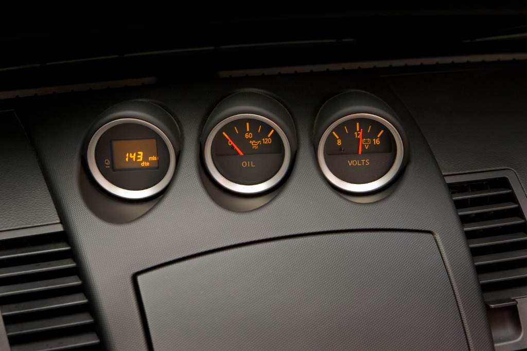 Close-up of the three center dashboard gauges in the Nissan 350Z displaying trip computer, oil pressure, and voltmeter