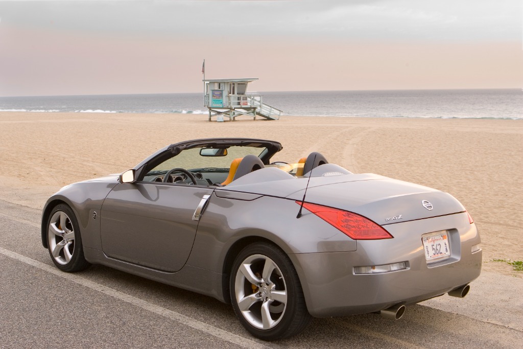 Silver Nissan 350Z Roadster parked seaside showing its sculpted rear deck and aerodynamic dual-fairing tonneau cover