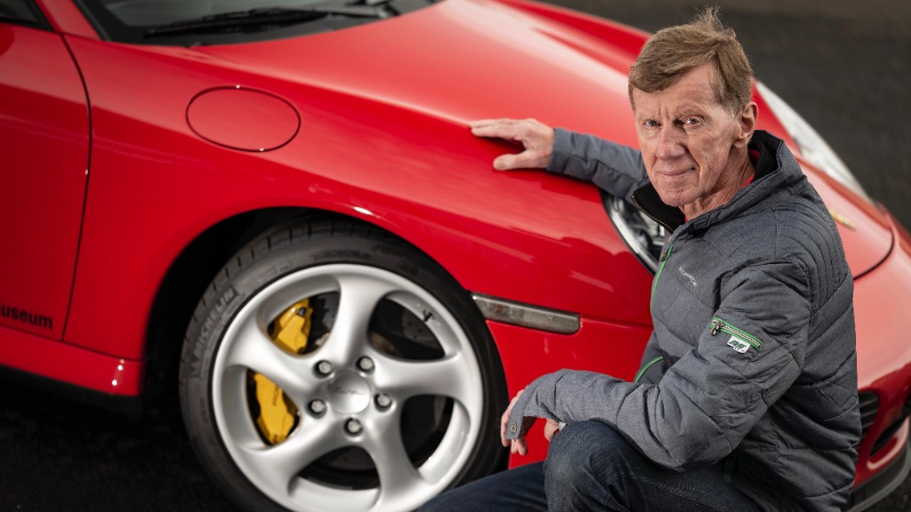 Walter Röhrl alongside the front wheel of a 996 Turbo S showcasing the yellow calipers of the PCCB carbon-ceramic brakes