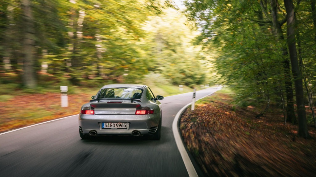 Grey Porsche 911 (996) Turbo S rear view driving dynamically through a mountain forest road